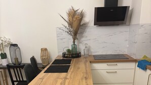 Eine kleine Küche mit Holzausziehtisch, weißen Schränken, einem integrierten Fernseher und einem Essbereich mit Stühlen und einem kleinen Tisch.