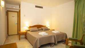 A hotel room with a double bed, two bedside tables, a chair, and a door. - HOTEL MAXIMUS (Las Navas del Marqués)