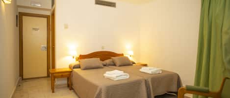 Una habitación de hotel con una cama doble, dos mesitas de noche, una silla y una puerta.