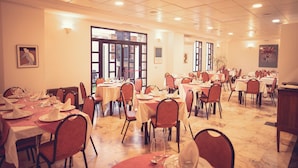A dining area with multiple tables and chairs, large windows, and framed artwork on the walls. - HOTEL MAXIMUS (Las Navas del Marqués)