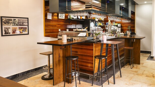 A bar area with a counter, stools, and a display case. - HOTEL MAXIMUS (Las Navas del Marqués)