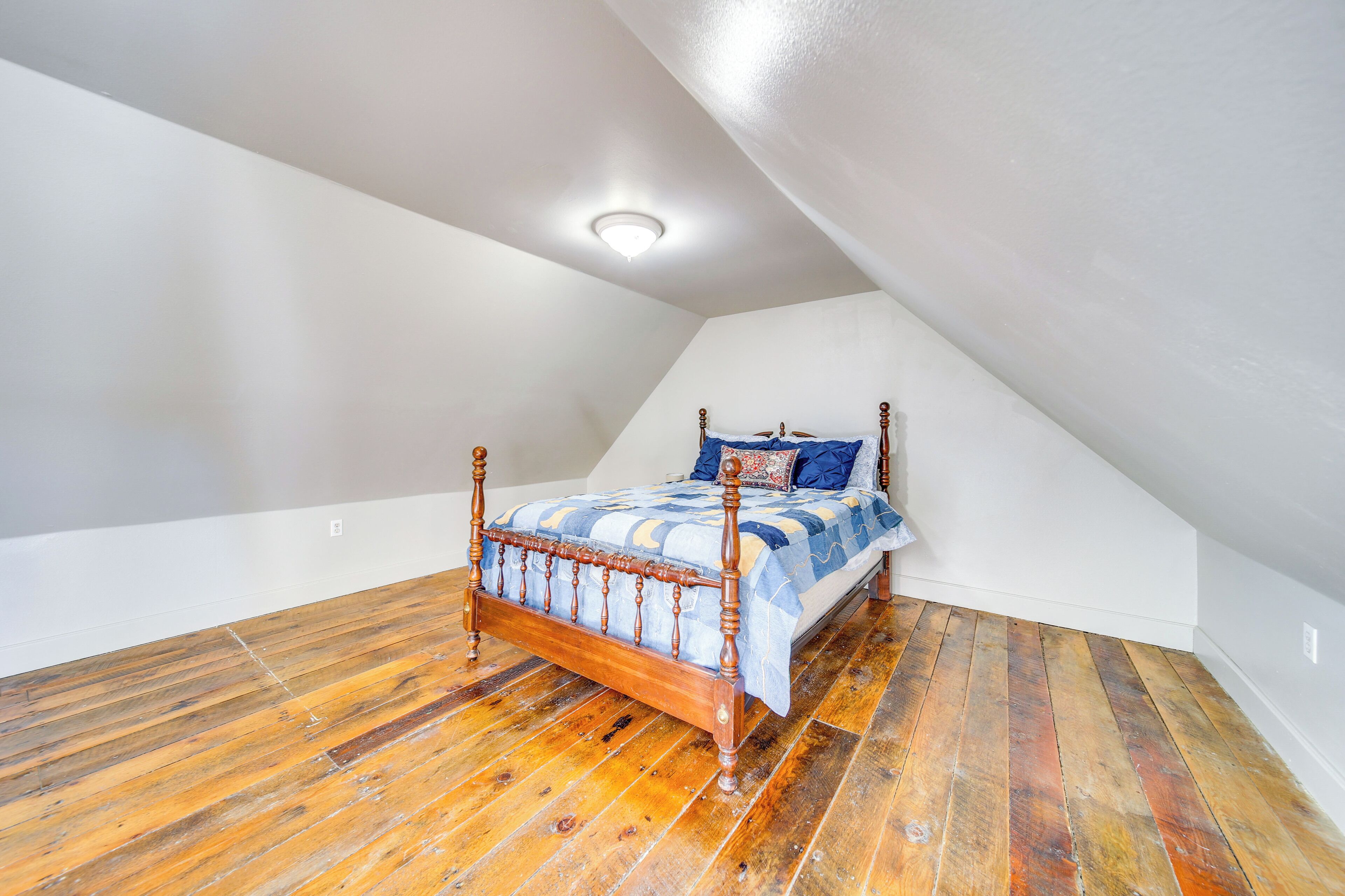 Une chambre avec un plancher en bois, un lit recouvert d’une couvre-lit à motifs bleus et blancs, et un plafond blanc doté d’un éclairage encastré.