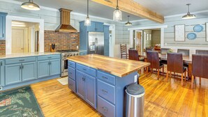 Una cocina amplia con armarios azules, una isla de madera, electrodomésticos de acero inoxidable y una zona de comedor con sillas de madera.