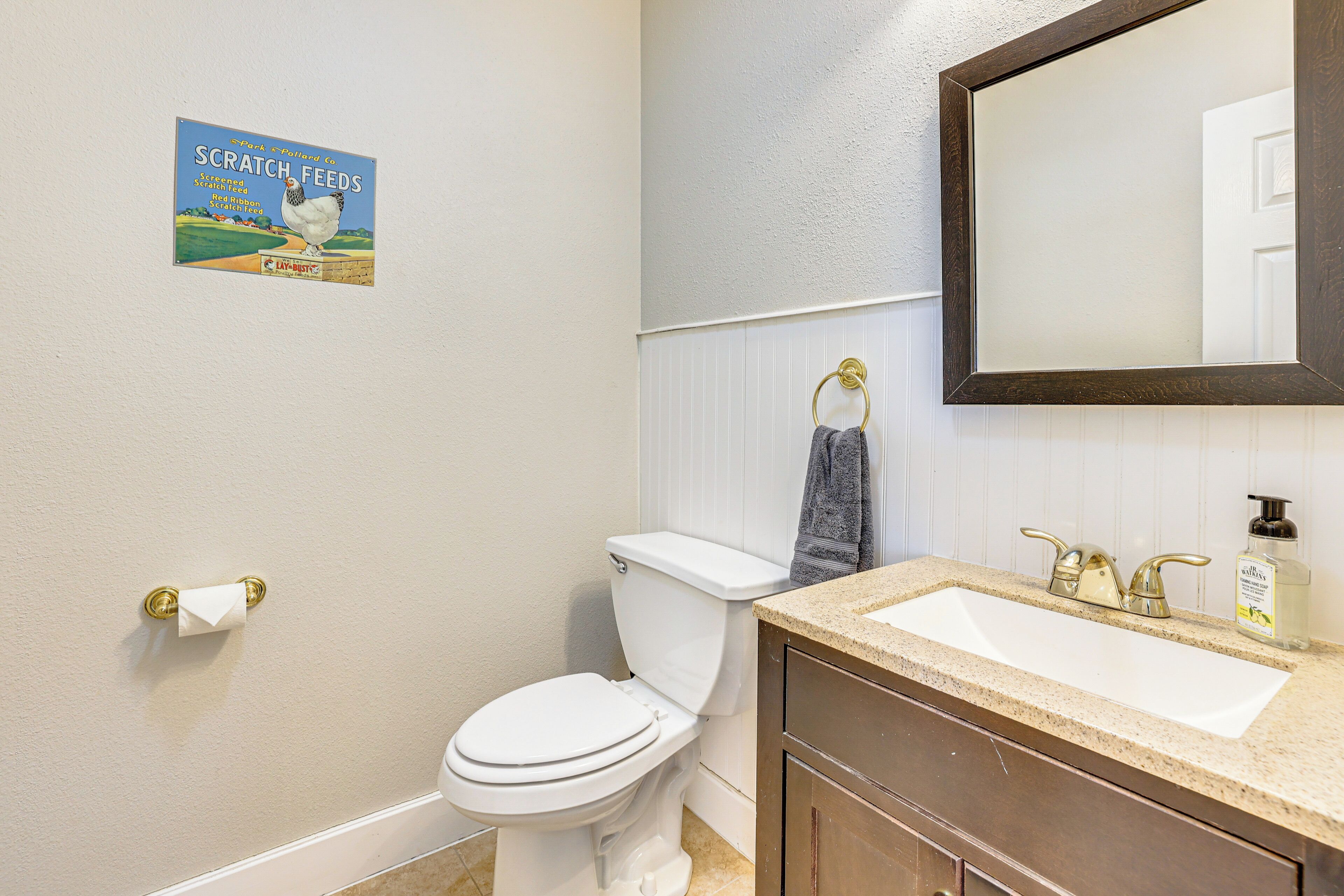 Een badkamer met toilet, wastafel en spiegel. Er hangt een handdoek aan de muur en een poster.