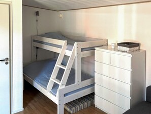 Ein Stockbett mit einer Stehle, eine weiße Kommode mit Schubladen und ein kleines Fenster mit Jalousie.