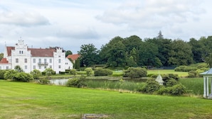 A large white building with a red roof, surrounded by a well-maintained lawn and a pond. - 4 Star Holiday Home in Yngsjo, Sverige (Yngsjo)