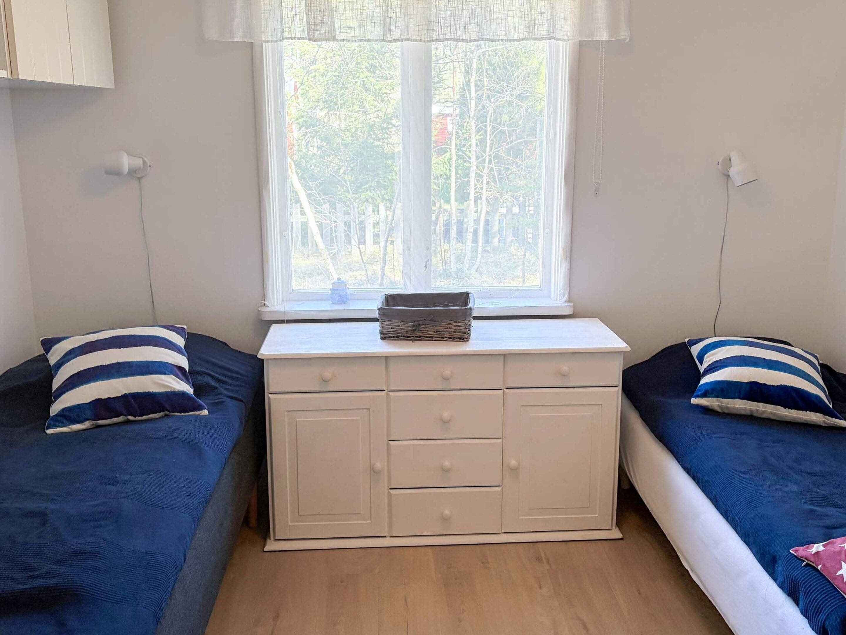 Una habitación con dos camas, un tocador blanco y una ventana con vista a árboles.