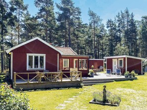 Una cabaña roja con un porche y mobiliario exterior, rodeada de un bosque.