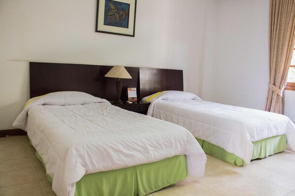 Una habitación de hotel con dos camas, una mesita de noche con lámpara y un cuadro enmarcado en la pared.