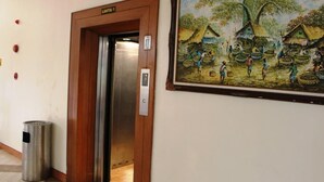 An elevator with a sign reading 'LANTAI 1' and a painting of a village scene on the wall. - Wisma Makara Universitas Indonesia (Jakarta)