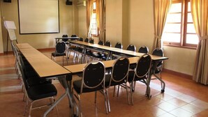 A conference room with a long table, chairs, a projector screen, and windows with curtains. - Wisma Makara Universitas Indonesia (Jakarta)