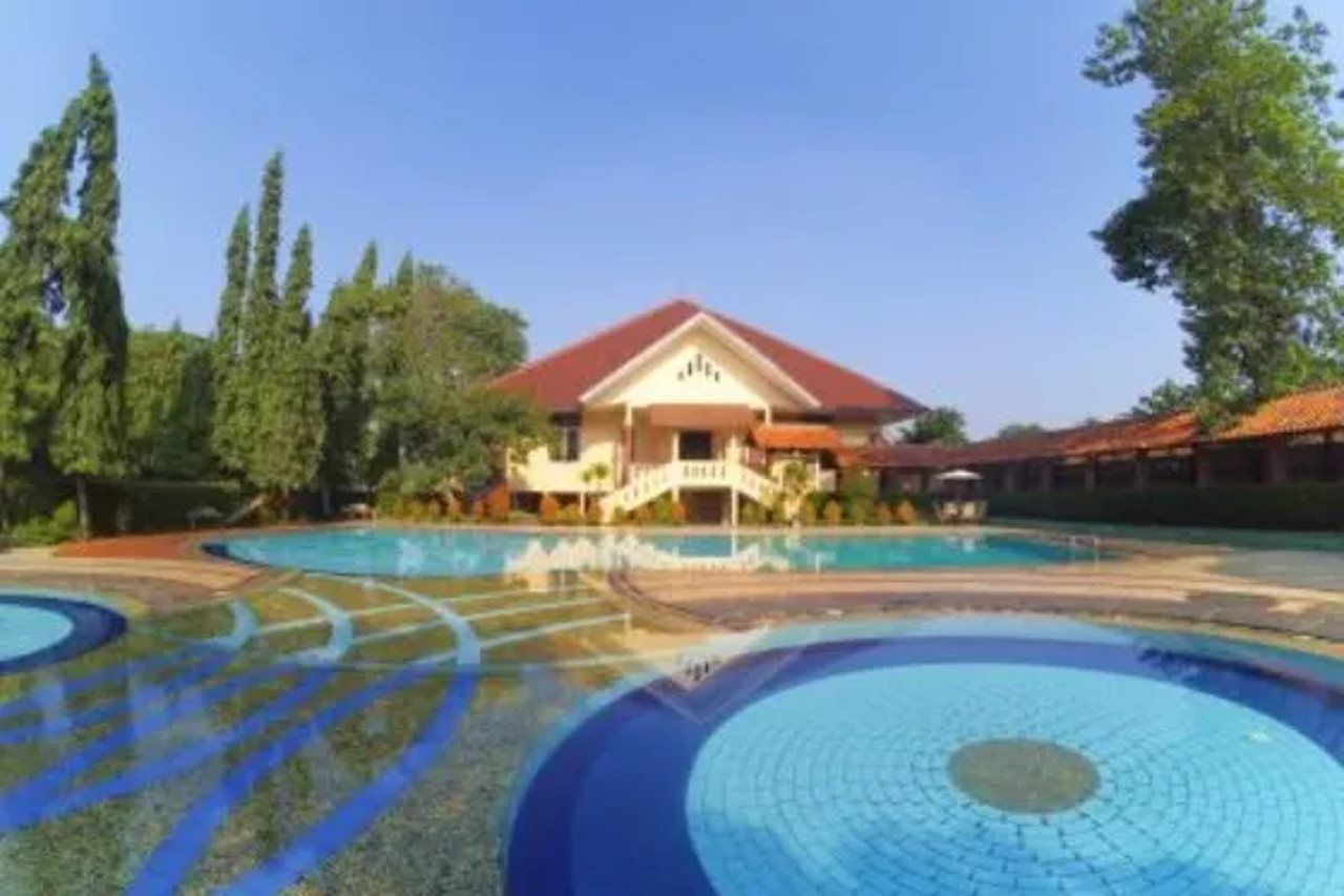 A hotel with a swimming pool, a covered outdoor area, and a building with a red roof.