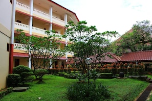 A multi-story building with balconies, a well-maintained garden with various plants, and a traditional tiled roof structure. - Wisma Makara Universitas Indonesia (Jakarta)
