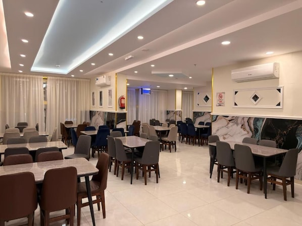 Ein geräumiges Restaurant mit mehreren Tischen und Stühlen, eingebossener Deckenbeleuchtung und Wandklimaanlagen.