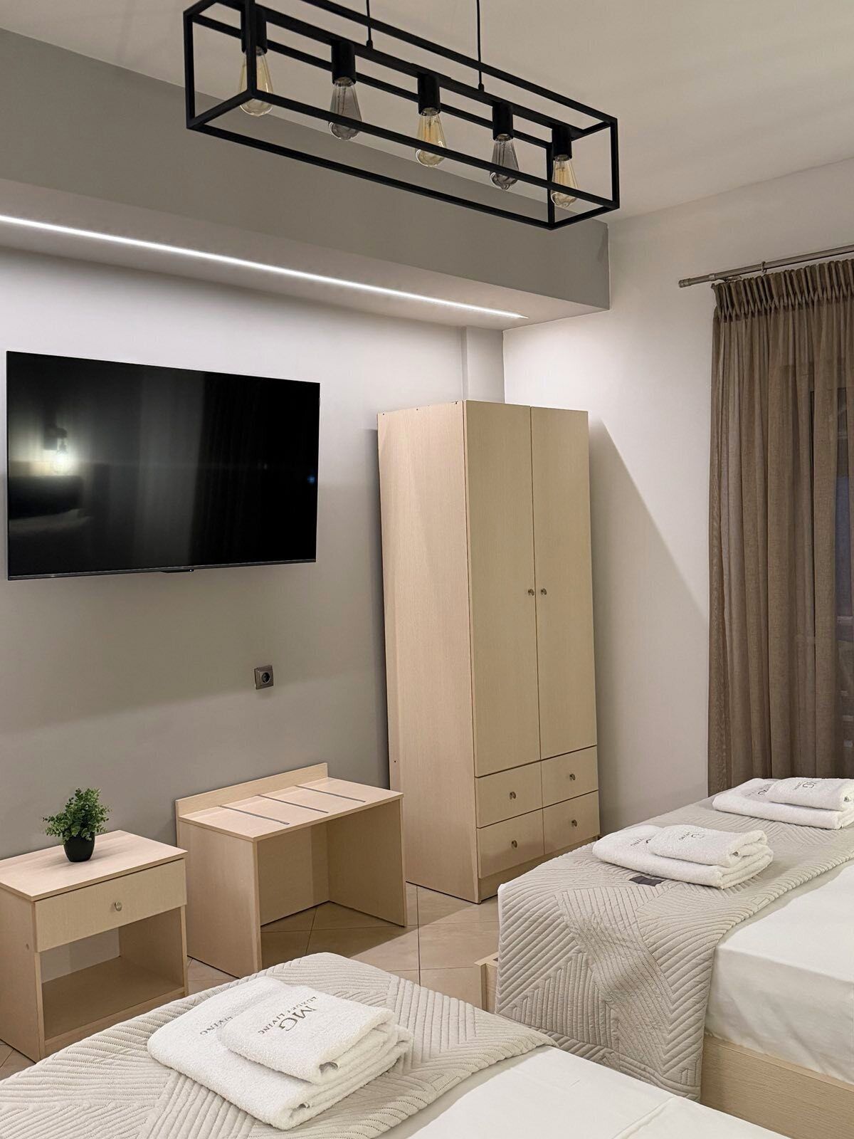 Una habitación de hotel moderna con televisor de pantalla plana, armario, escritorio y dos camas con toallas.