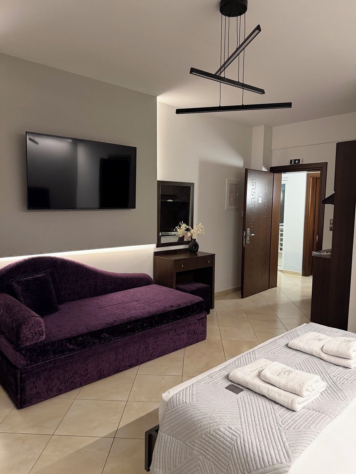 A modern bedroom with a sofa bed, a flat-screen TV, a desk, and a wardrobe.