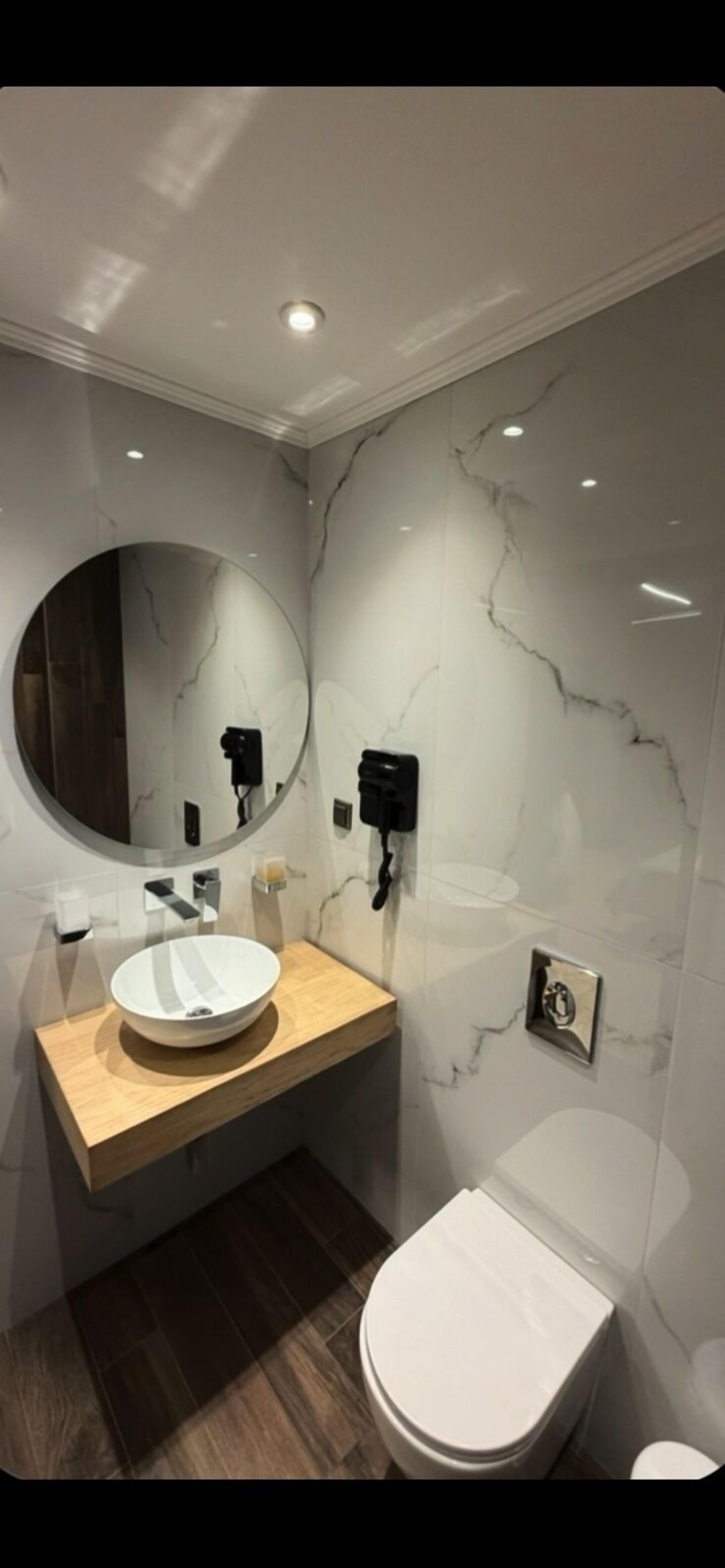 A modern bathroom with a round mirror, a white sink, and a toilet.
