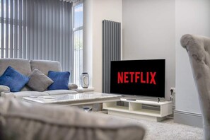 Un salon moderne avec un canapé, une table basse et un téléviseur affichant le logo « NETFLIX ».