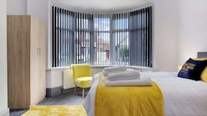 A bedroom with a large bed, a wooden wardrobe, a radiator, a yellow chair, and a window with blinds. - 3 Bedroom With Backyard, 10 Min to City Centre (Tyne and Wear)