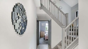 A hallway with a modern abstract wall art, a staircase with white railings, and a glimpse of a bedroom with a bed and dresser. - 3 Bedroom With Backyard, 10 Min to City Centre (Tyne and Wear)