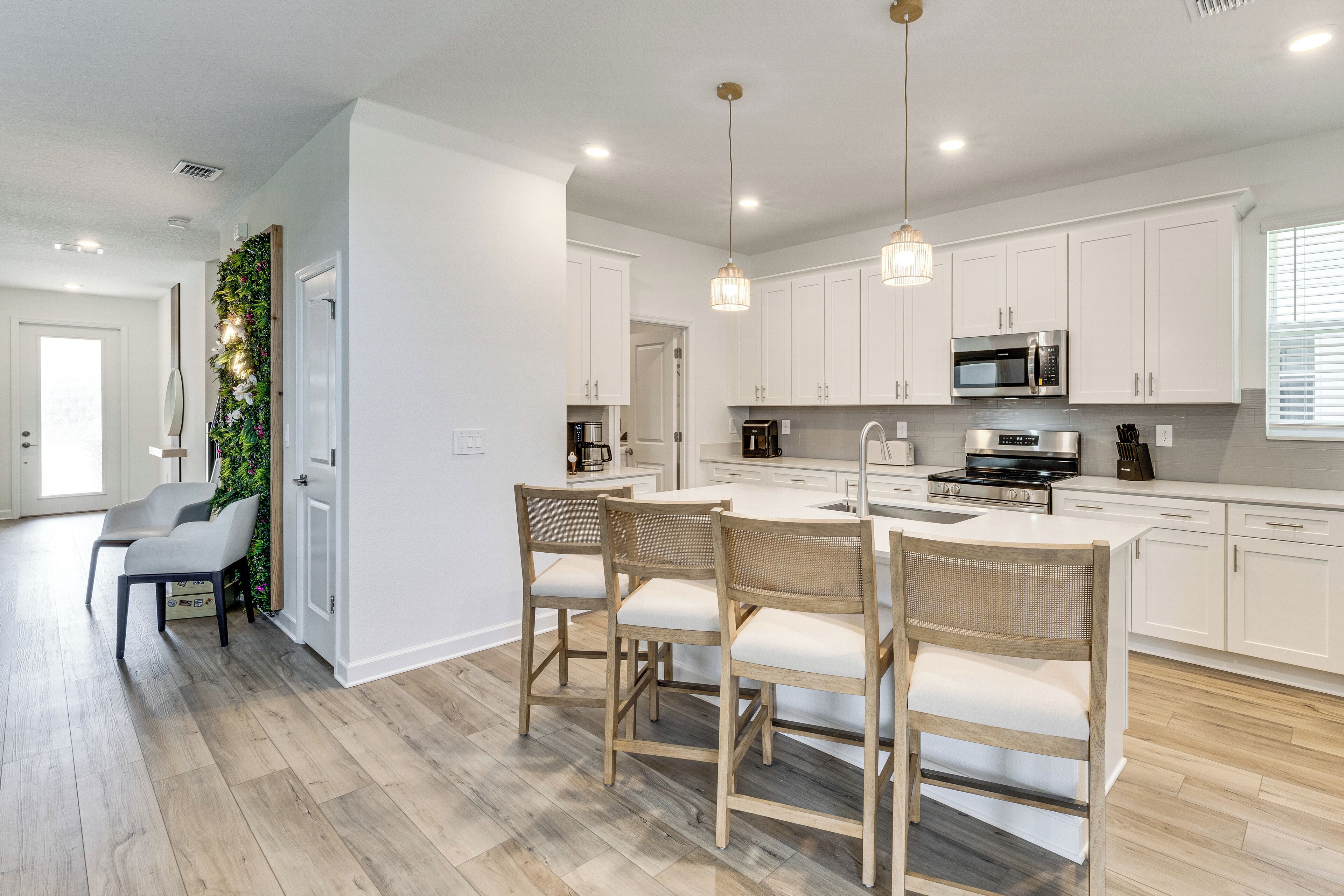 A modern kitchen with white cabinets, a central island, and a dining area with wicker chairs.