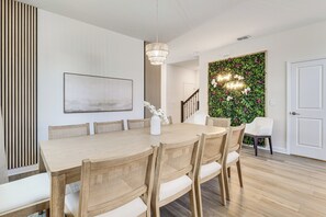 Ein Essbereich mit Holztisch und -stühlen, einer Chandelüster, einer Treppe und einer Wand mit grünem Blattschmuck.