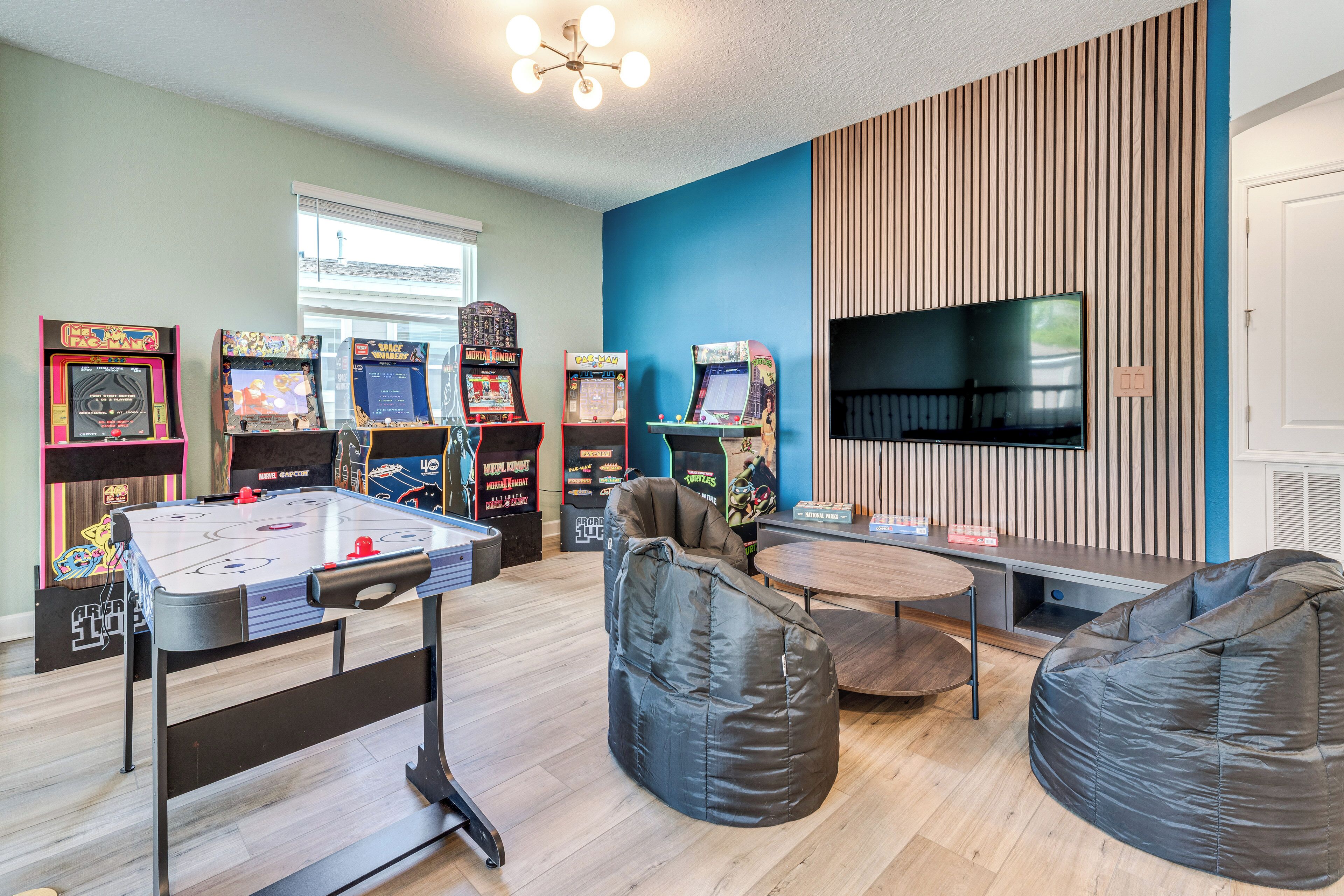 A room with a foosball table, bean bag chairs, arcade games, and a flat-screen TV.
