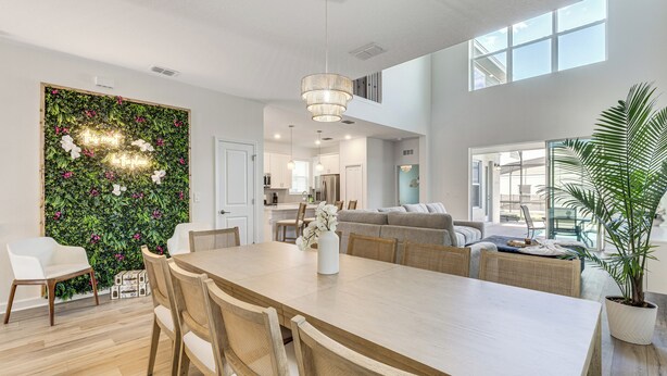 A spacious living area with a dining table, chairs, a sofa, and a large window. - Poolside Bliss & Epic Game Rooms! Gem in Kissimmee (Kissimmee)