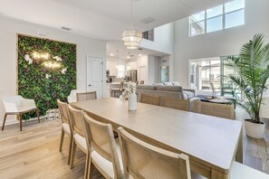 A spacious living area with a dining table, chairs, a sofa, and a large window. - Poolside Bliss & Epic Game Rooms! Gem in Kissimmee (Kissimmee)