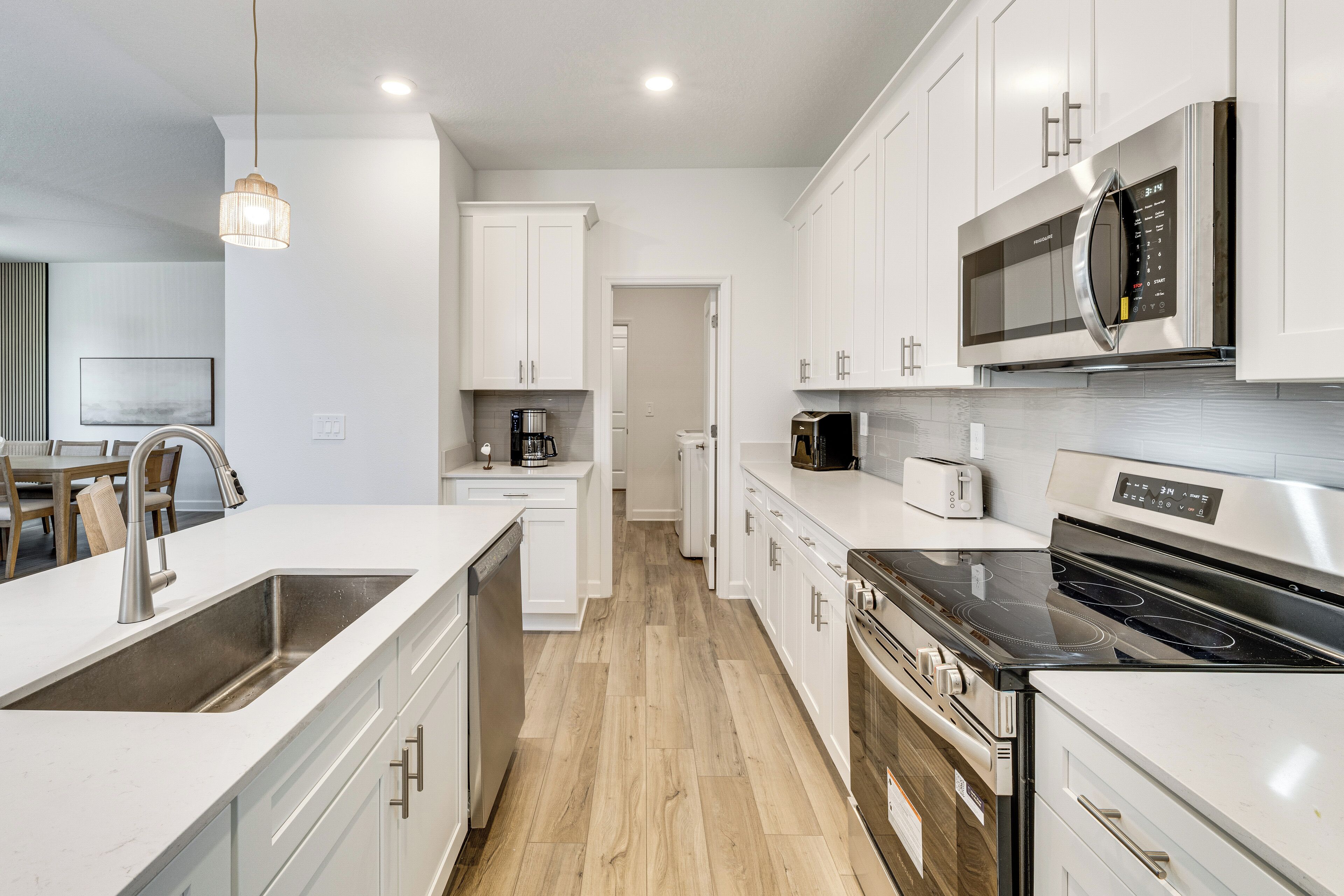 A modern kitchen with white cabinetry, stainless steel appliances, and a wooden floor.
