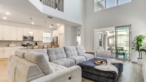 A spacious living area with a sectional sofa, a dark ottoman, and a dining table. - Poolside Bliss & Epic Game Rooms! Gem in Kissimmee (Kissimmee)