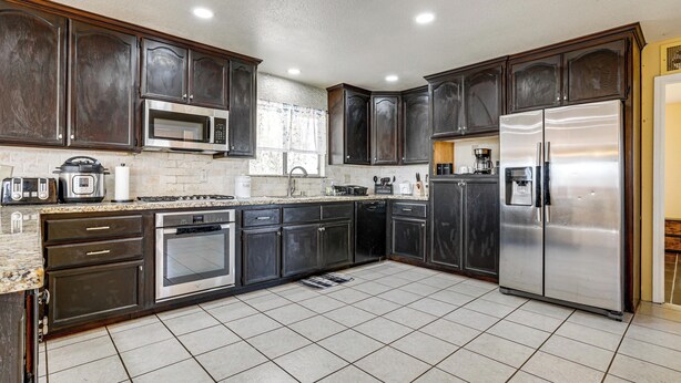 A modern kitchen with dark cabinetry, stainless steel appliances, and a tiled floor. - Wine Country Retreat in Galt w/ Vineyard Views (Galt)