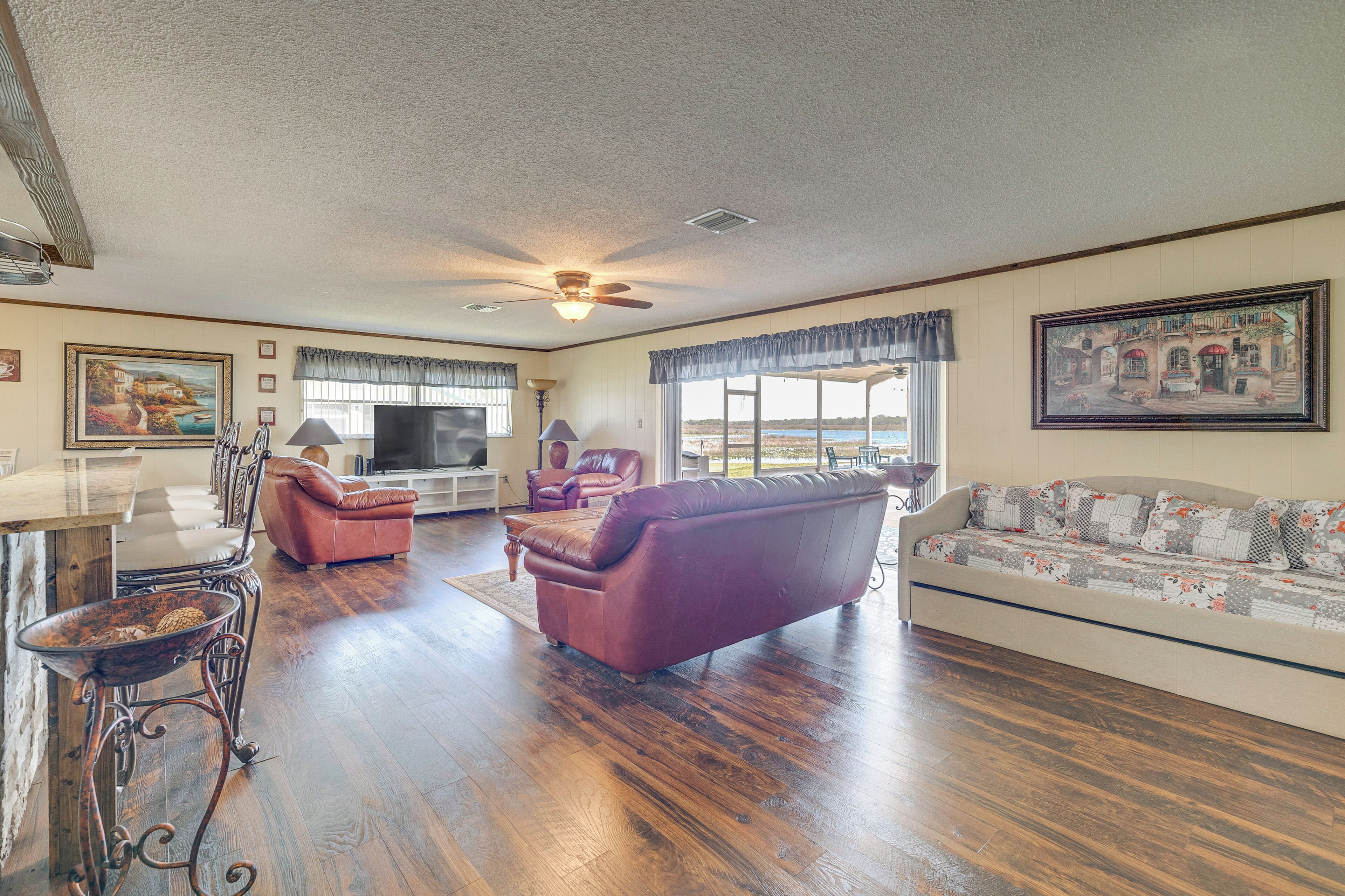 A spacious living room with hardwood flooring, a ceiling fan, a television, a fireplace, and a large window with a view.