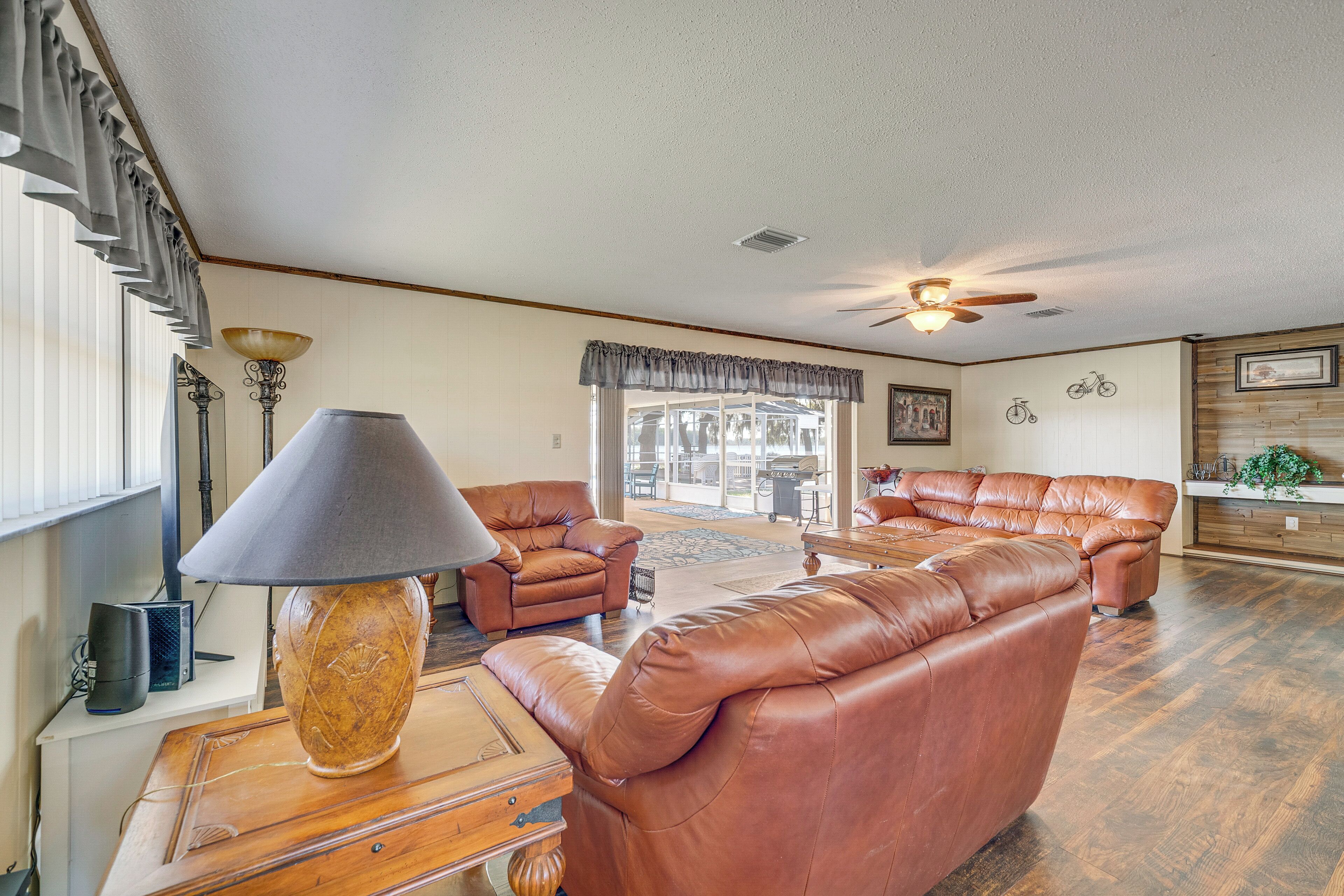 A spacious living room with leather sofas, a wooden coffee table, a lamp, and a ceiling fan.