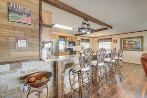 A kitchen with a stone backsplash, wooden cabinets, a bar area with metal chairs, and a dining table. - Lakefront & Poolside! Family Retreat in Hernando (Hernando)