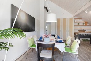Un coin repas avec une table dressée pour quatre personnes, un grand tableau accroché au mur et une table de baby-foot à l’arrière-plan.