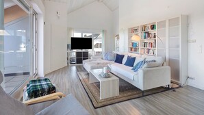 A spacious living room with a white sofa, a coffee table, a bookshelf, and a television. - Zwergenweg Apartment – 140 sqm, Nature, Tranquility & Stunning Views over the Rhine Valley (Badenweiler)