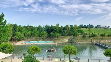 A serene lakeside setting with a sandy beach, a small dock, and a bridge over the water.