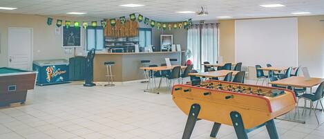Una habitación con mesa de fútbol, mesa de billar y zona de bar con refrigerador y mostrador.