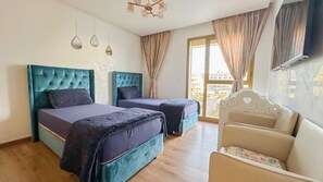 Hotellihuone, jossa on kaksi sänkyä, sohva, televisio ja ikkuna, jossa on verhot.