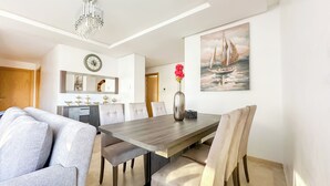A modern dining area with a wooden table, cushioned chairs, a vase with flowers, and a sailboat painting on the wall. - The Carrousel Residence - Rabat (Rabat)
