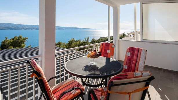 Un balcone con tavolo e sedie, affacciato su un corpo d'acqua e delle colline.