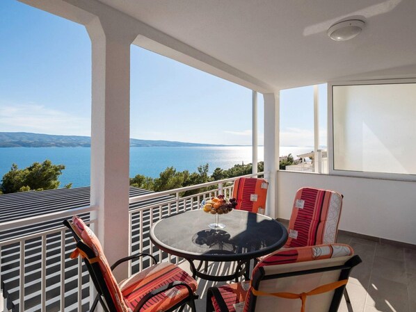 A balcony with a table and chairs, overlooking a body of water and hills. - Estate With Sea Views Near Omis (Omis)