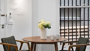 Een kamer met een ronde houten tafel, twee stoelen, een vaas met bloemen en uitzicht door een traliesraam.