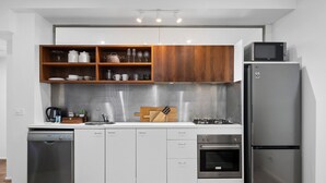 Een moderne keuken met witte kasten, een roestvrijstalen koelkast, een vaatwasser en houten planken boven het aanrecht.