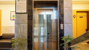 An elevator with a glass door, a reception area with a sofa, and a potted plant. - Treebo Premium Inn 62 (Noida)
