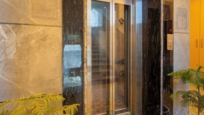An elevator with glass doors, a marble wall, and a potted plant. - Treebo Premium Inn 62 (Noida)