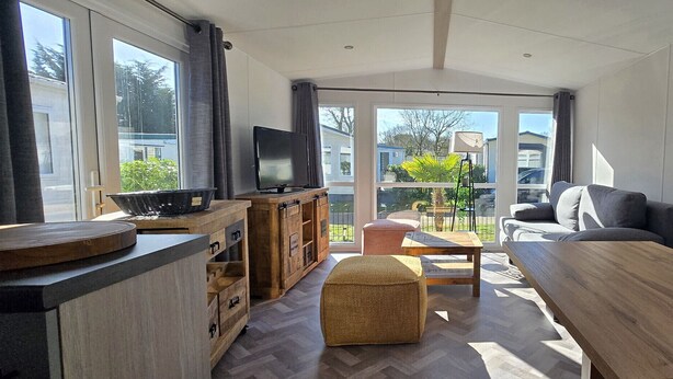 A modern living room with a wooden coffee table, a sofa, a television, and a kitchen area with cabinets and a countertop. - Vakantiepark Kijkduin - 838 (Den Haag)
