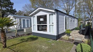 A mobile home with a large window, a patio with outdoor furniture, and a well-maintained lawn. - Vakantiepark Kijkduin - 838 (Den Haag)