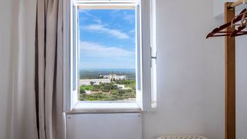 A room with a window, a radiator, a wooden hanger, and a white plastic stool.